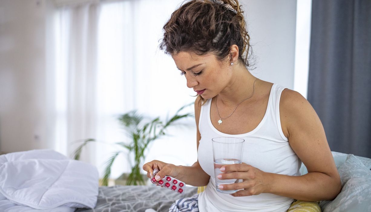 Junge Frau, hält ein Glas Wasser in der Hand und eine Packung Tabletten.