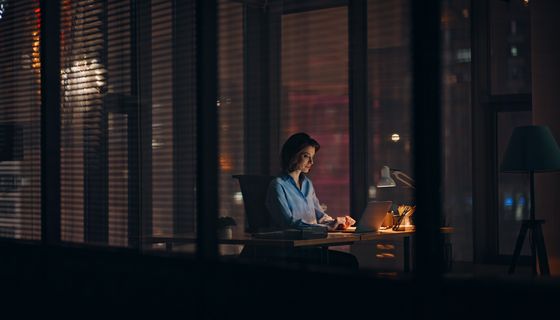 Frau, sitzt abends im Büro und arbeitet.