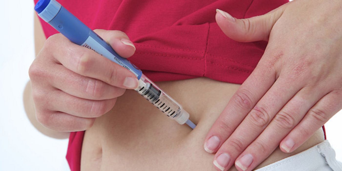 Fotoausschnitt Bauch, in den von einer Frauenhand Insulin gespritzt wird