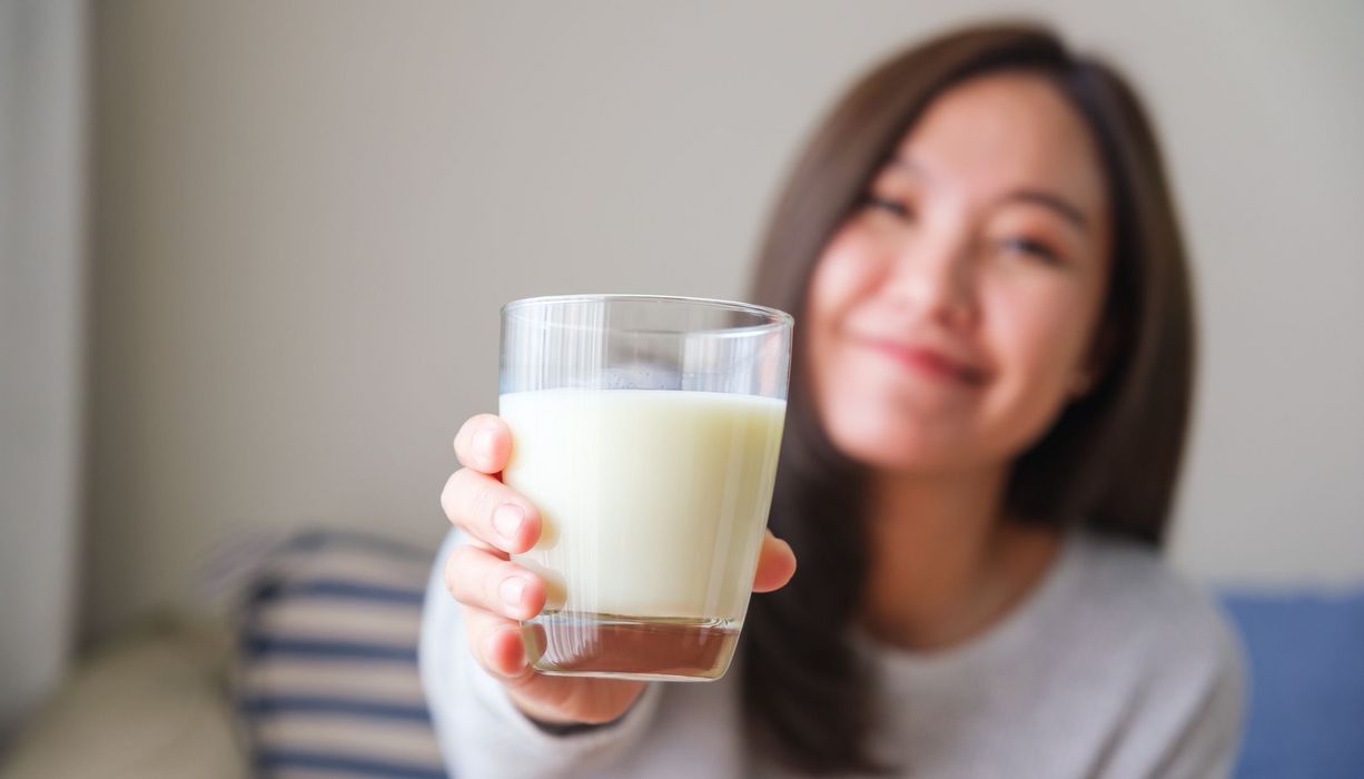 Frau, hält ein Glas Milch in die Kamera.