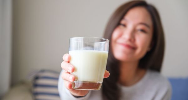 Frau, hält ein Glas Milch in die Kamera.