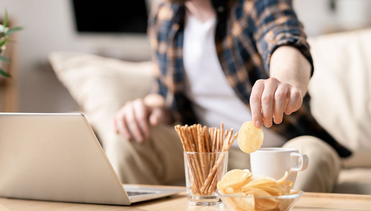 Mann, sitzt am Laptop und isst Chips.