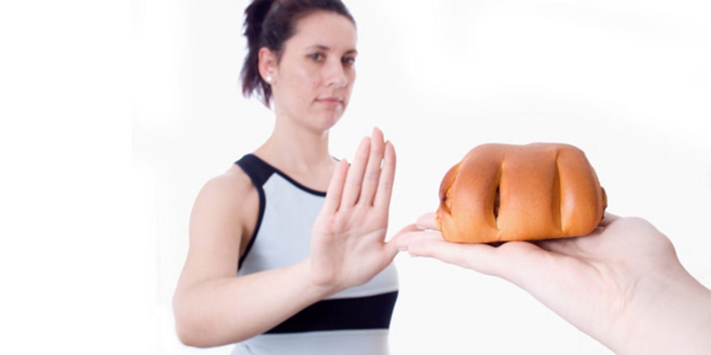 Junge Frau weist das ihr auf einer Hand angebotene Backwerk mit einer abweisenden Geste zurück