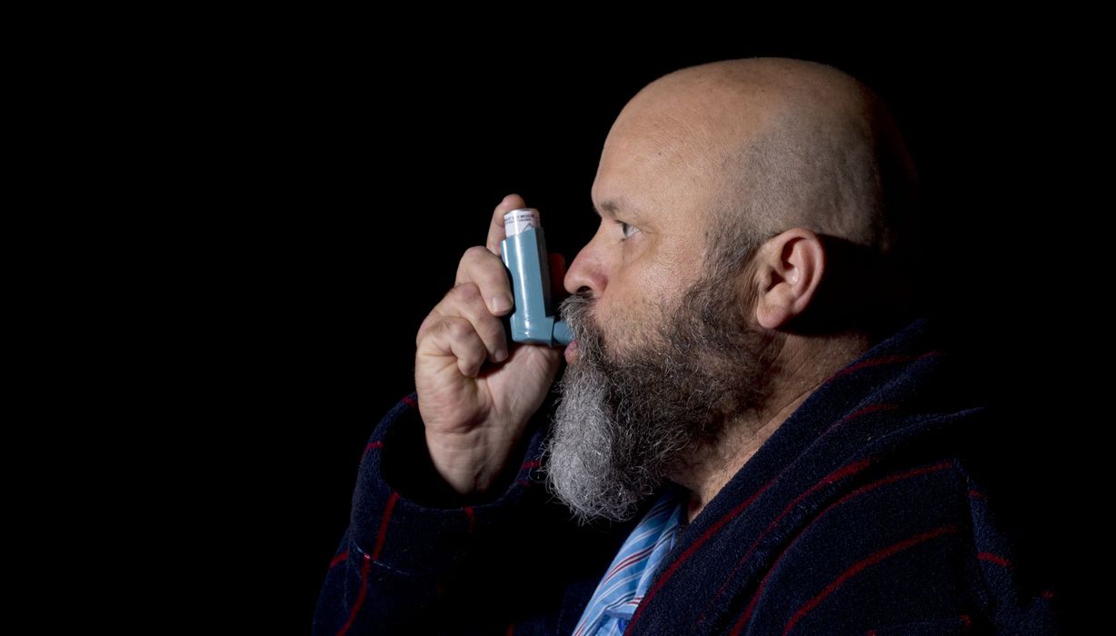 Bärtiger Mann inhaliert Asthmaspray.