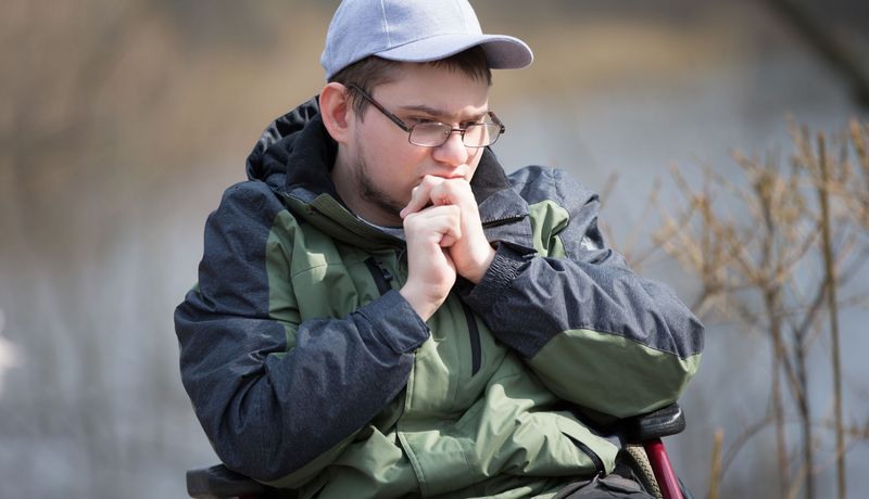 Ein junger Mann im Rollstuhl blickt traurig.