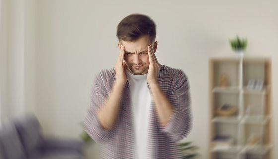 Mann fasst sich an die Schläfe und blickt nach unten. Im unteren Bereich ist das Bild verwischt, als hätte sich die Kamera schnell bewegt.