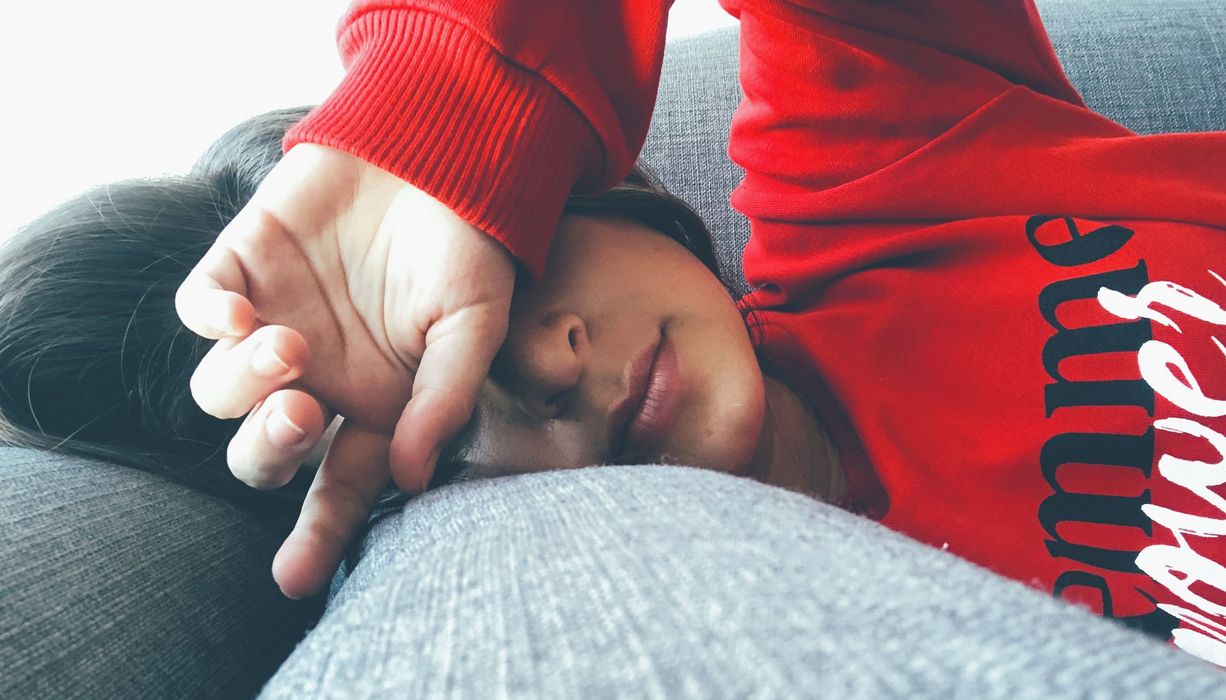 Frau, liegt im Bett und legt ihre Hand über die Stirn.