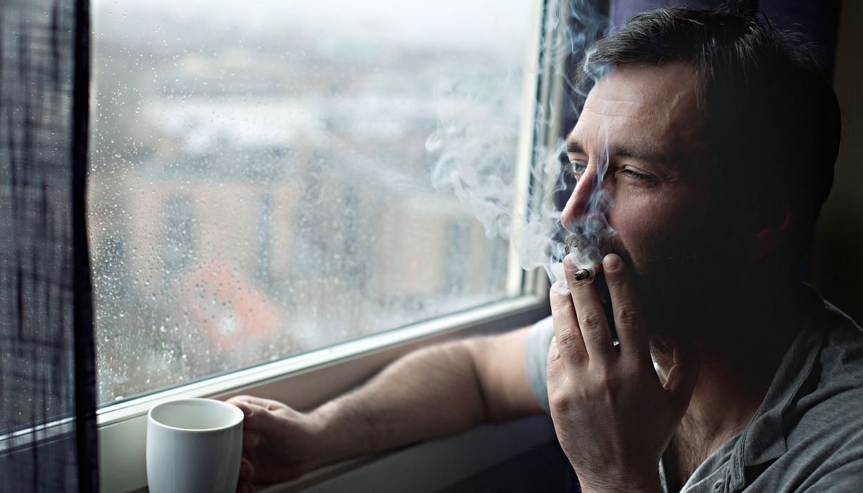 Mann sitzt am Fenster und raucht.