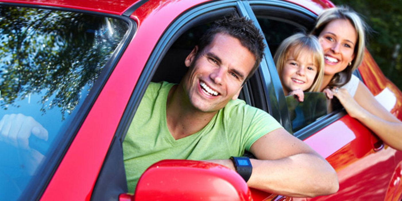 Vater, Mutter, Kind lehnen sich aus einem roten Auto