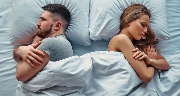 Paar, liegt Rücken an Rücken im Bett, beide sind grimmig.