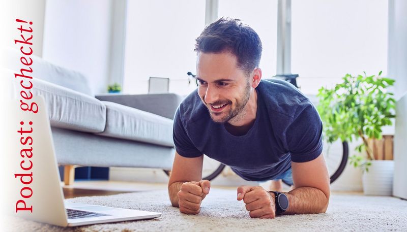 Junger Mann macht Sport im Wohnzimmer vor dem Laptop.