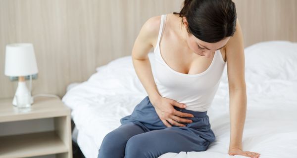 Junge Frau sitzt auf dem Bett und hält sich den Unterleib.