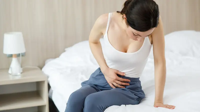 Junge Frau sitzt auf dem Bett und hält sich den Unterleib.