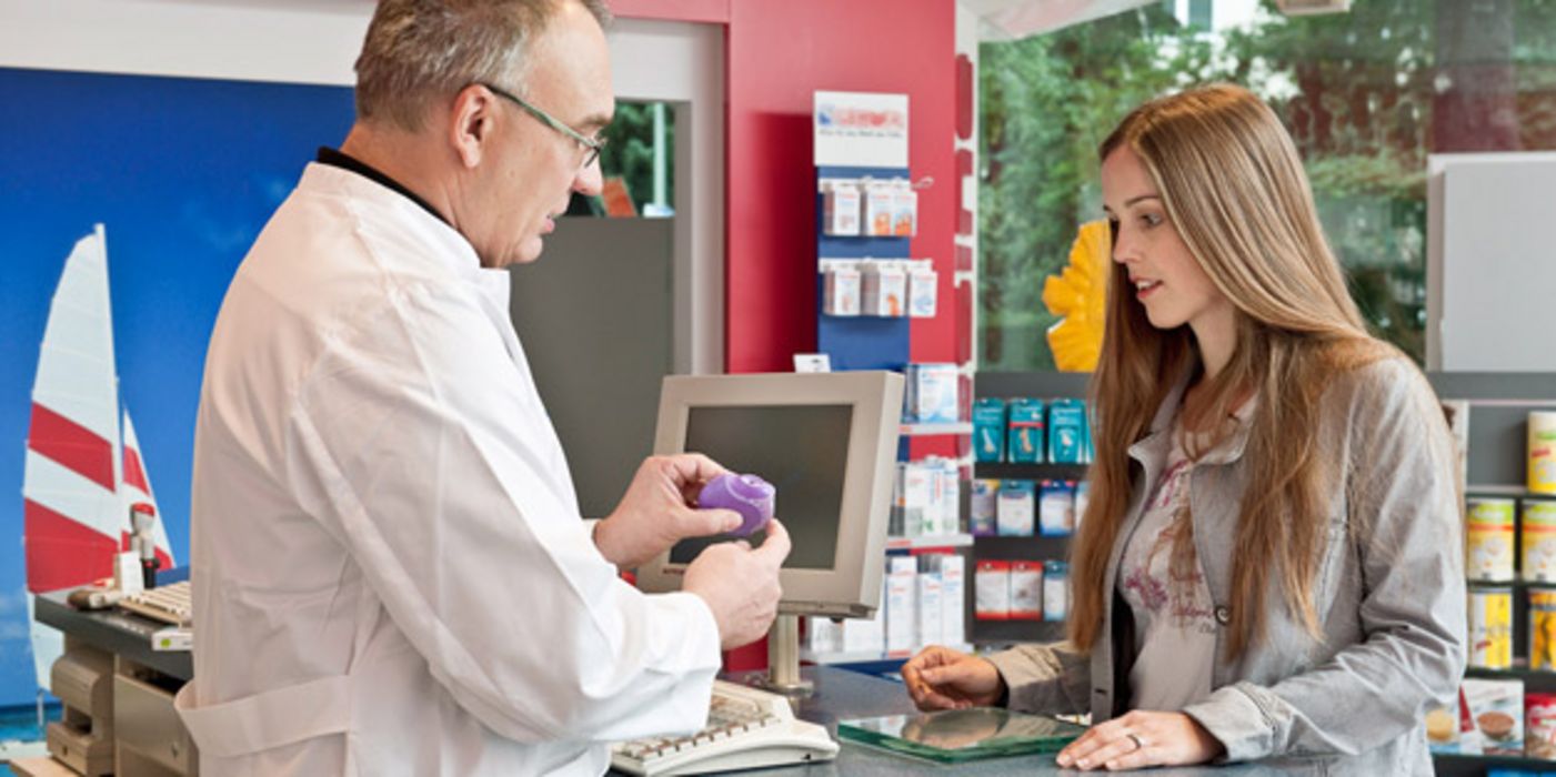 Apotheker erklärt junger Kundin, wie ein Asthma-Inhalator funktioniert.