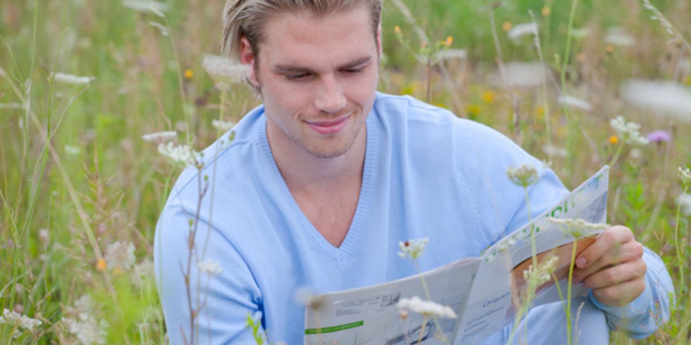 Mann sitzt auf einer Blumenwiese und liest