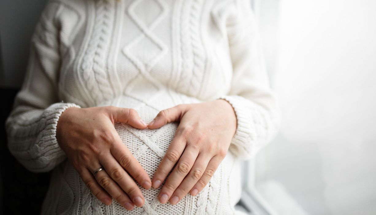 Frau, hält beide Hände an ihren Babybauch.