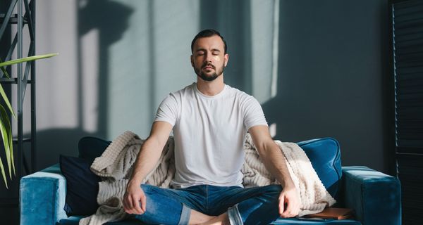 Mann, sitzt mit geschlossenen Augen auf einer Couch und meditiert.