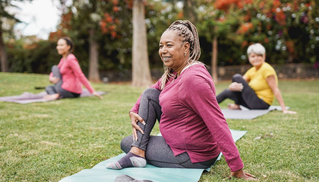 Ältere Frau, macht Yoga draußen mit einer Gruppe.