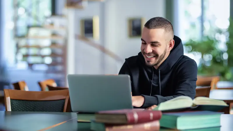 Junger Mann, sitzt am Laptop.