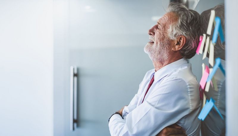 Senior, lehnt sich im Büro an die Wand und sieht erschöpft aus.