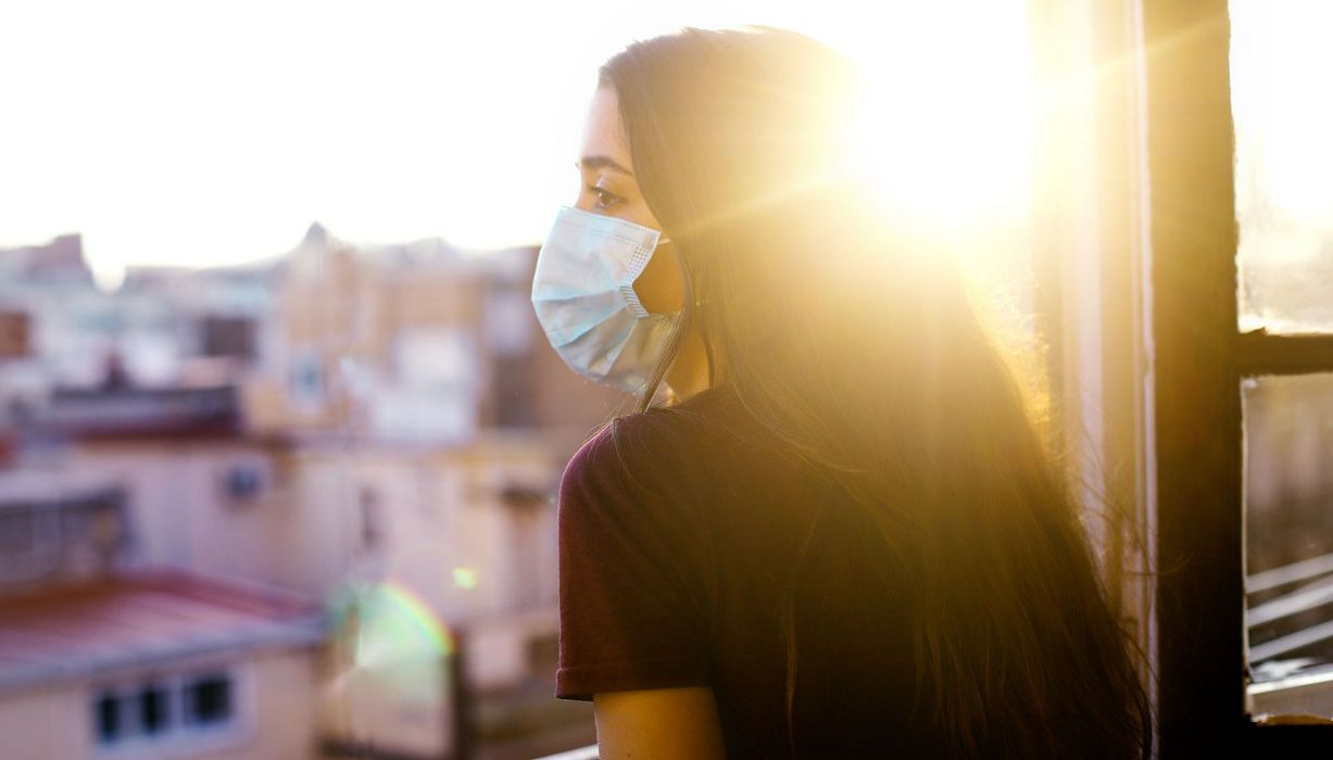 Junges Mädchen mit Maske, schaut aus dem Fenster in die Ferne..