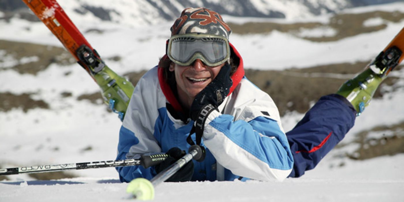 Skifahrer mir Skibrille liegt auf dem Bauch im Schnee, die Skier sind gekreuzt