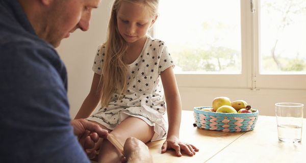 Vater, klebt seiner Tochter ein Pflaster auf das Knie.