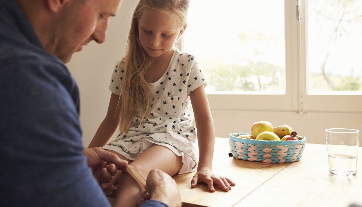 Vater, klebt seiner Tochter ein Pflaster auf das Knie.