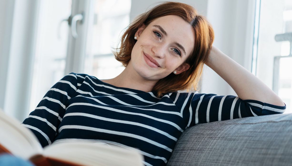 Frau, sitzt auf der Couch und liest ein Buch.