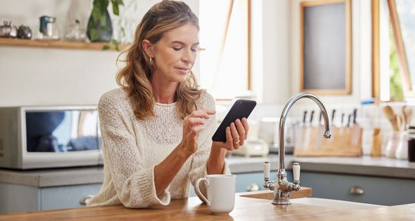 Frau steht in der Küche und schaut auf ihr Smartphone.