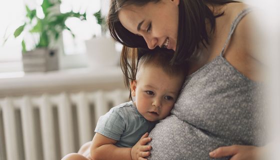 Kleiner junge horcht am Bauch seiner schwangeren Mutter.