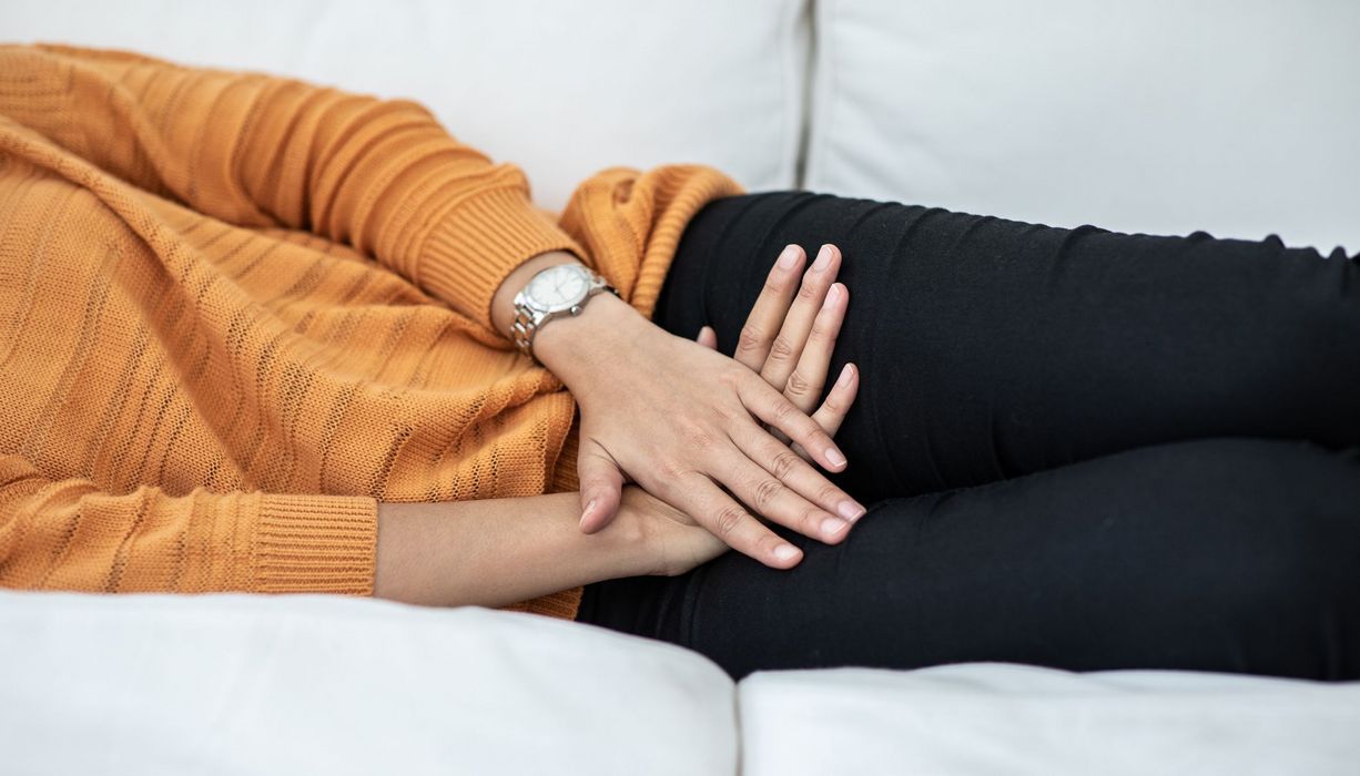 Frau, liegt auf einer Couch, hält ihre Hände über den Unterbauch.