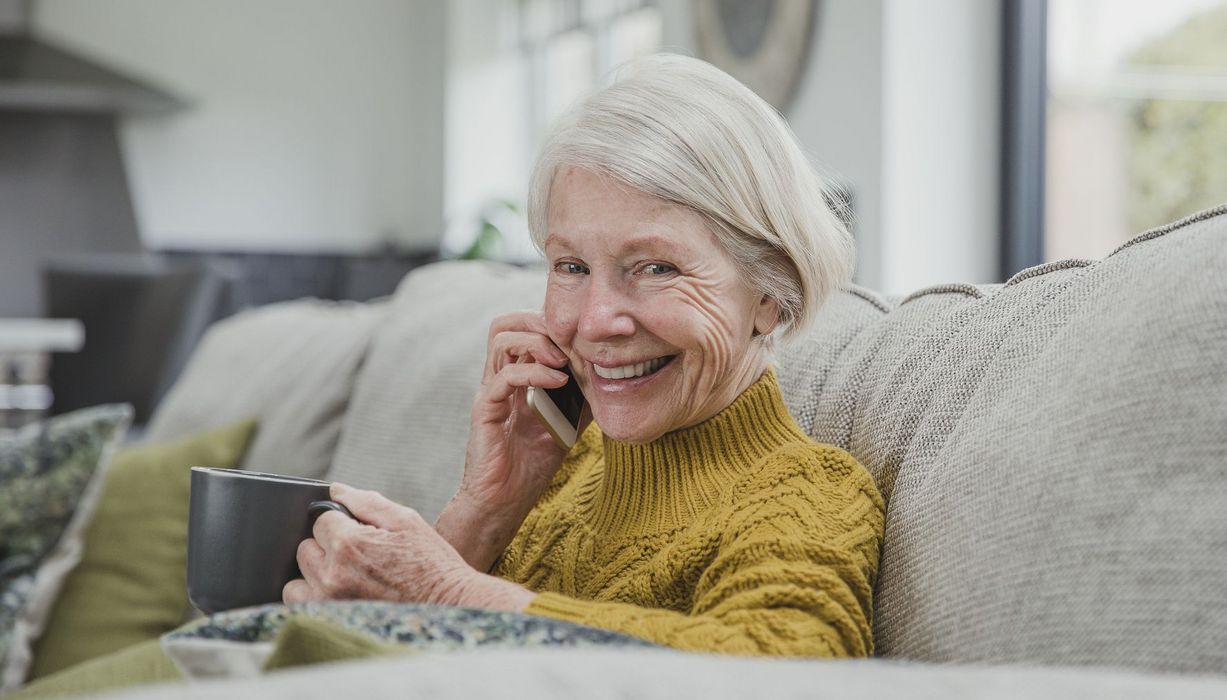 Seniorin mit Kaffee telefoniert auf dem Sofa.