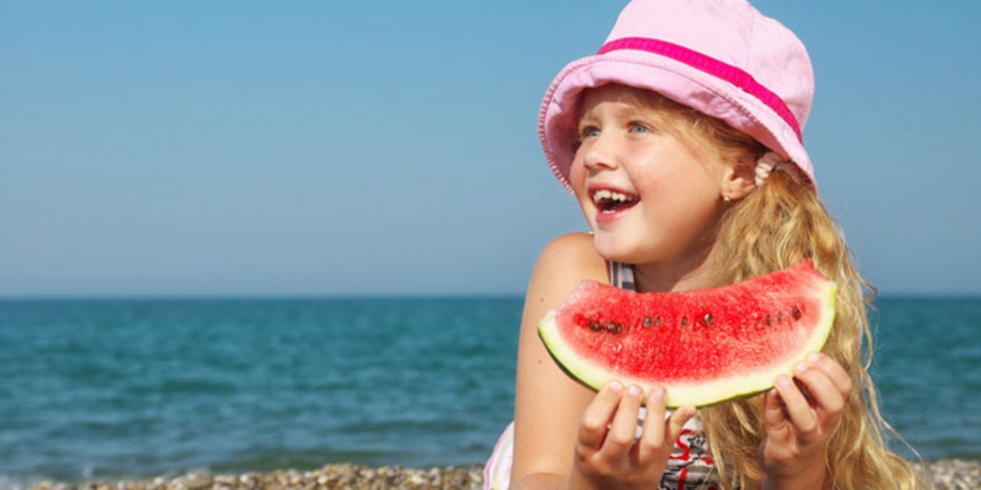 Mädchen liegt am Strand und isst ein Stück Wassermelone