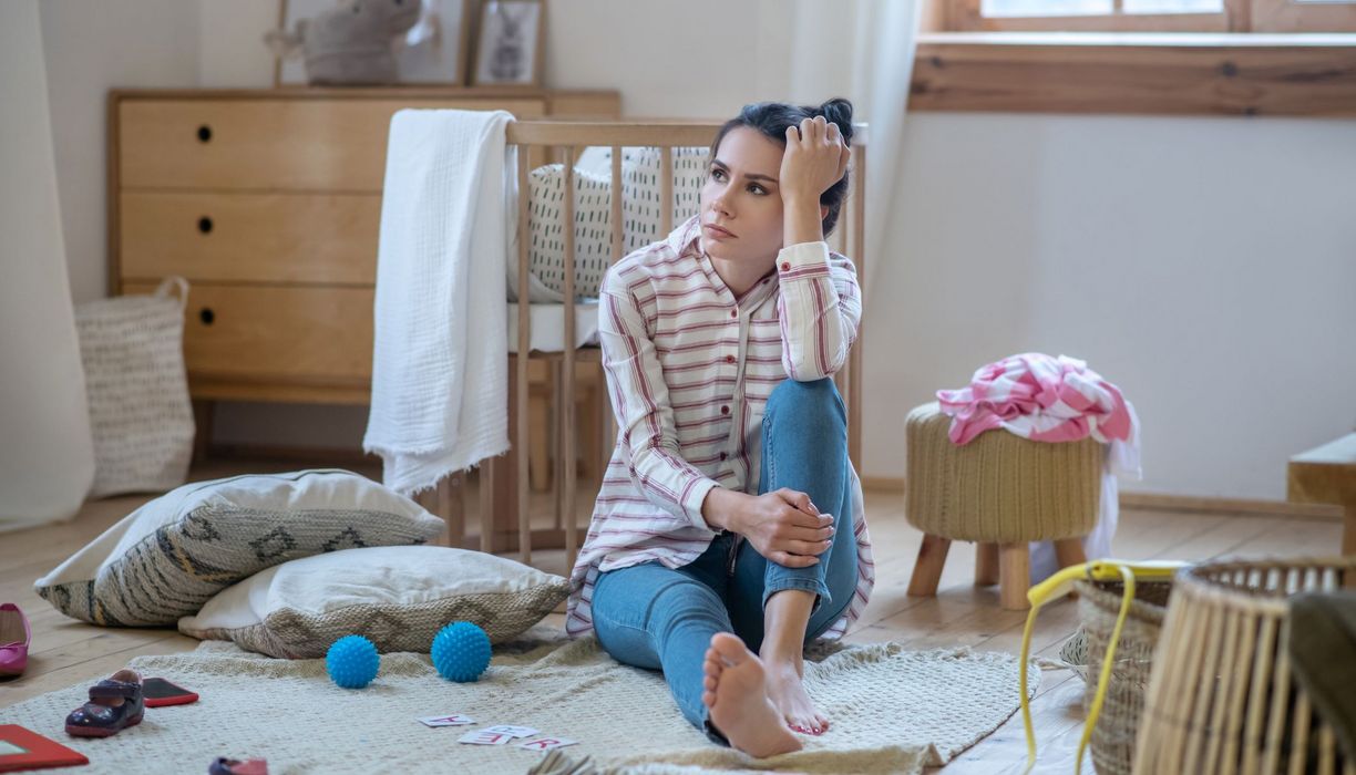 Junge Frau, sitzt verzweifelt im Kinderzimmer.