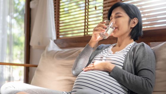 Schwangere Frau, trinkt ein Glas Wasser.