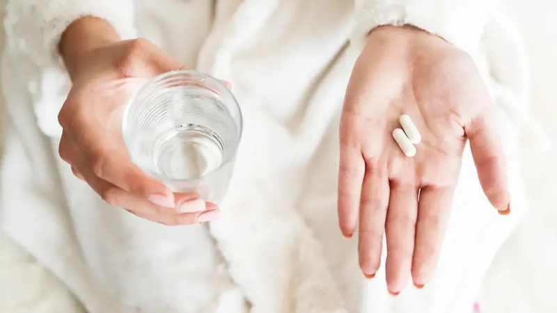 Hände halten Tabletten und ein Glas Wasser