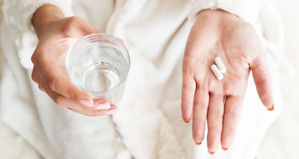 Hände halten Tabletten und ein Glas Wasser