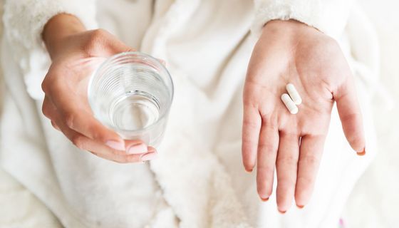 Hände halten Tabletten und ein Glas Wasser