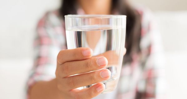 Frau, hält ein Glas Wasser in die Kamera.