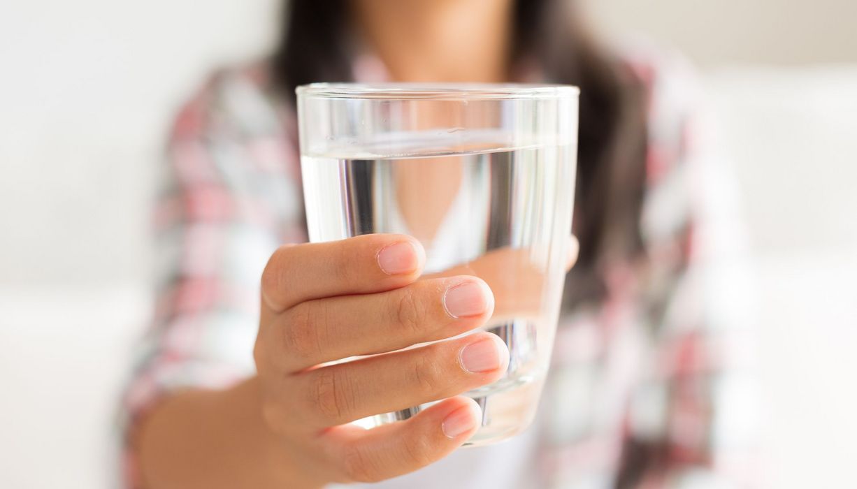 Frau, hält ein Glas Wasser in die Kamera.