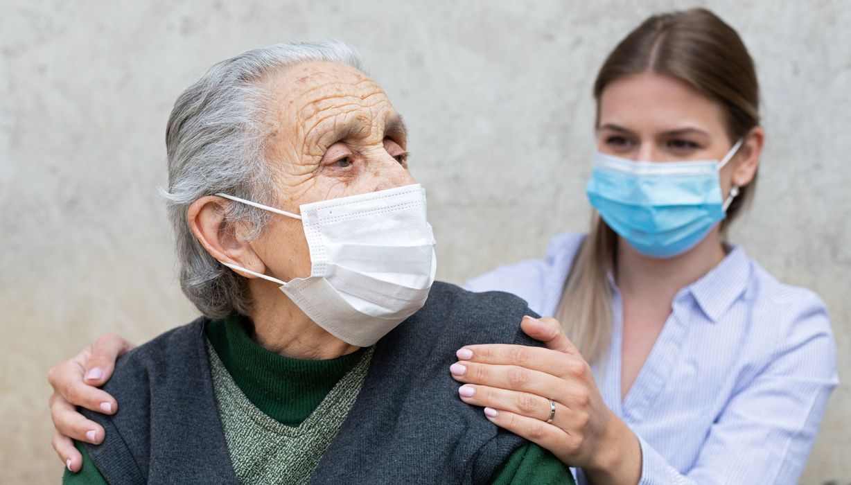 Seniorin und Pflegerin, beide tragen eine Maske.