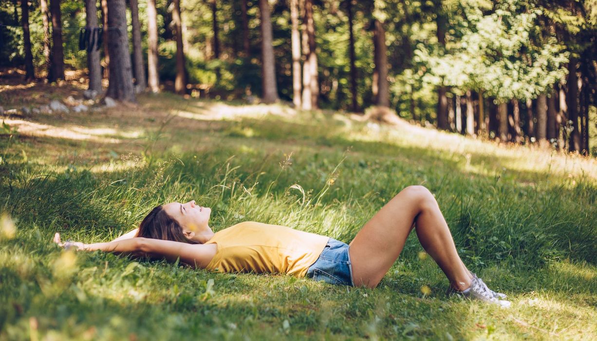 Junge Frau, liegt im Sommer auf einer Wiese.