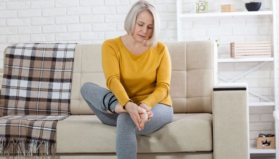 Frau sitzt auf dem Sofa uns hält sich den Fuß.