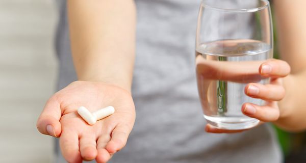 Kind, hält zwei Tabletten in der Hand und ein Glas Wasser in der anderen Hand.