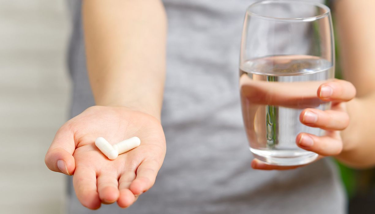 Kind, hält zwei Tabletten in der Hand und ein Glas Wasser in der anderen Hand.