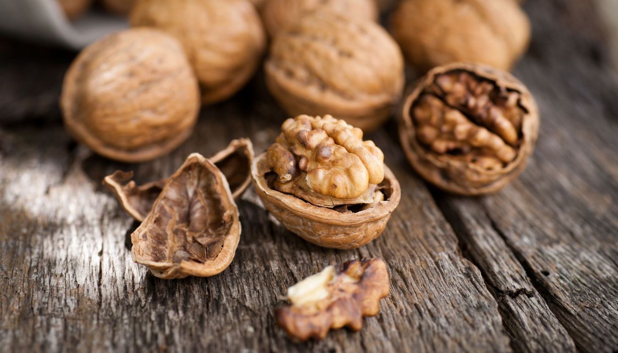 Walnüsse - teilweise geöffnet - liegen auf einem Holztisch verteilt