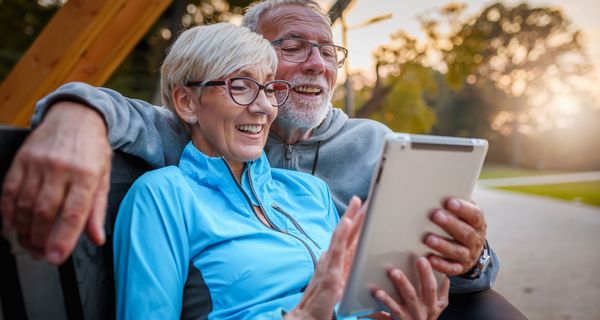 Ein älteres Pärchen, sitzt auf einer Bank und schaut lächelnd auf ein Tablet.