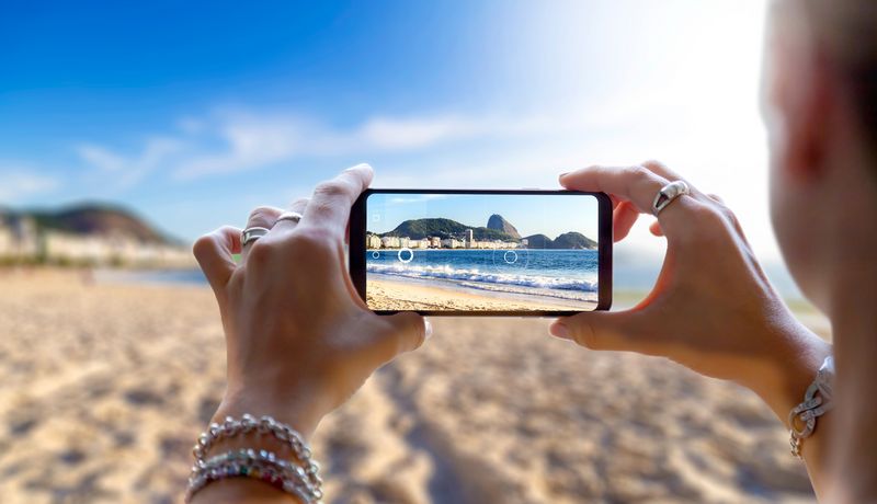 Eine Frau nimmt ein Foto von einem Strand mit einem Smartphone.