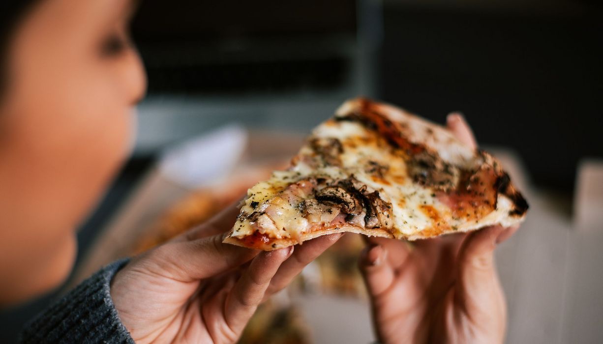 Frau, hält ein Stück Pizza in der Hand.